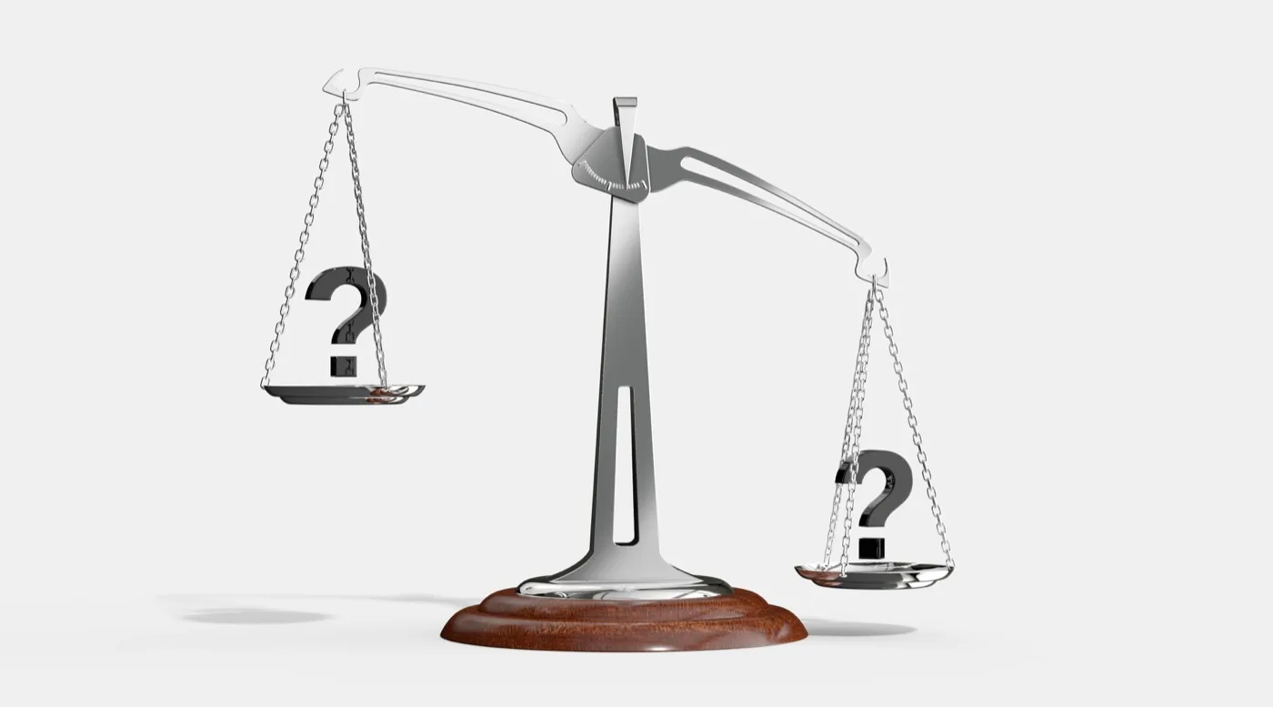 A metal scale on a wooden stand with a white background that has a question mark on each of the dishes on the side of the scale.