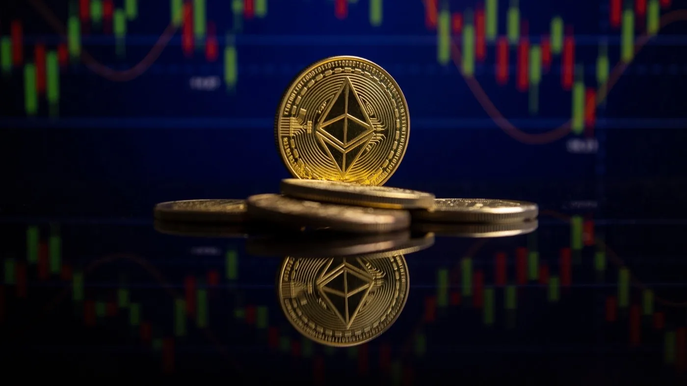 A shiny ethereum crypto gold coin sitting up on its edge with other coins laying beneath it with the market chart in behind them.