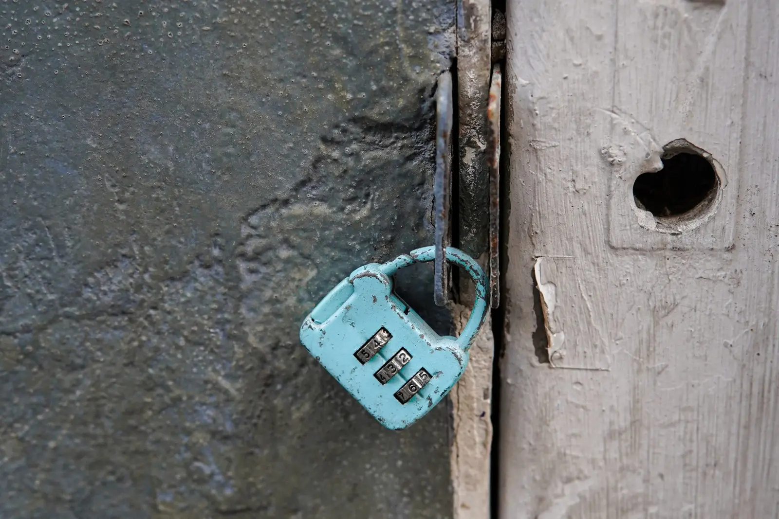 Worn turquoise combination padlock hanging from a rusty latch, illustrating the Muse chat sharing privacy pause